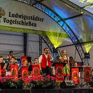 Das Bild zeigt die Frankenwald Musikanten Windheim auf der Bühne bei ihrem Auftritt. Sie tragen rote Westen.