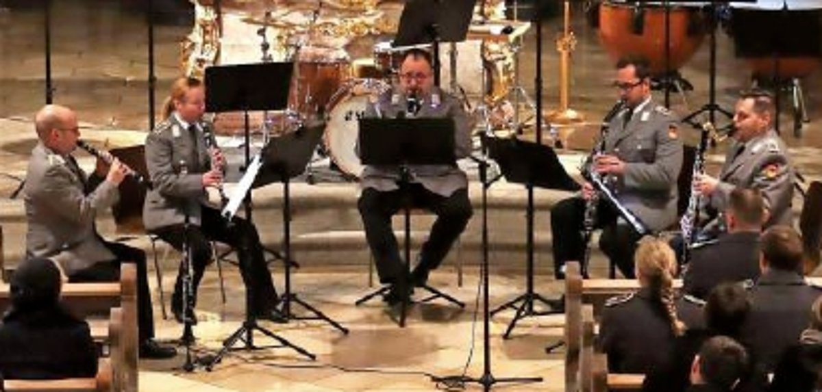 Das Bild zeigt einen Teil des Heeresmusikkorps in Uniform während eines Konzertes. Jeder spielt sein Instrument und schaut in seine Notenblätter.