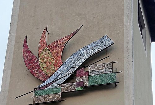 Betonturm mit einem Mosaik aus kleine verschieden farbigen Glasteilchen zeigen Stein, Wasser und Feuer