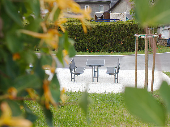 Auf dem Foto schaut man zwischen gelb blühenden Blüten auf die neue Sitzgruppe mit zwei Bänken und einem Tisch.