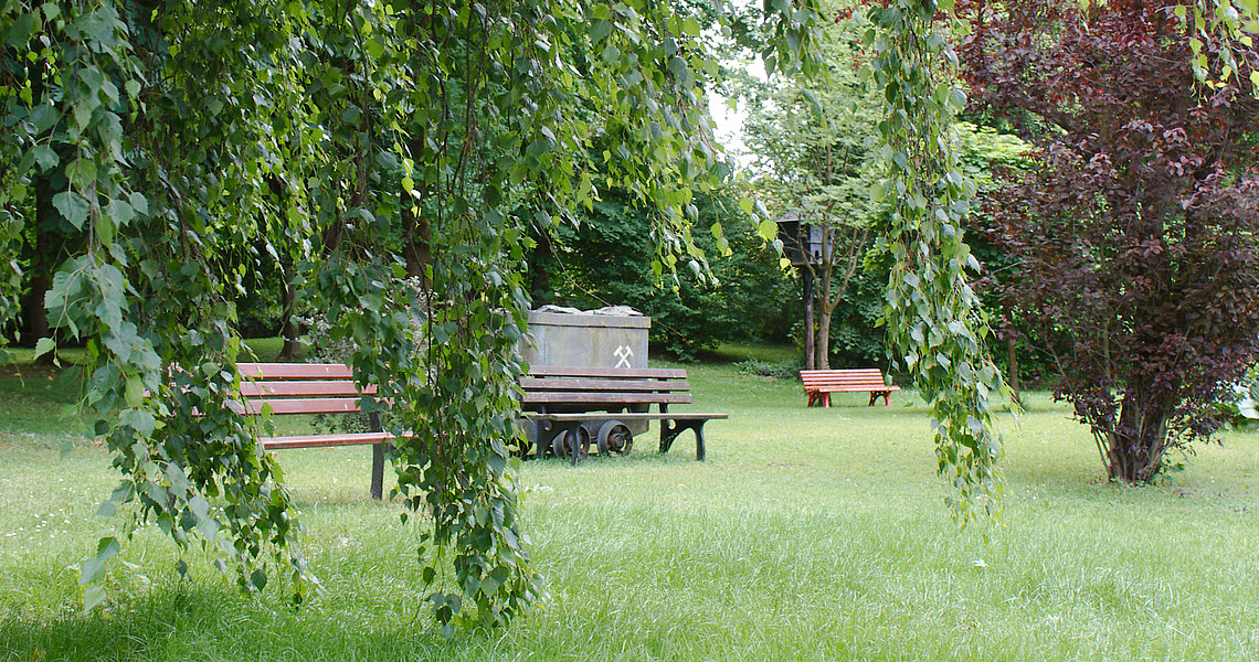 Das Foto zeigt den kleinen Park in Lauenhain mit einer Bank und einem Grubenwagen. 