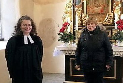 Pfarrerin und eine Seniorin stehen mit Abstand vor einem Kirchenaltar