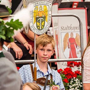 Das Foto zeigt einen Jungen, der das Schild der Ludwigsstädter Schützen trägt. Das Schild zeigt das Wappen der Schützengesellschaft. Der Junge schaut ganz konzentriert und trägt ein blau-weiß kariertes Hemd und eine Lederhose. 