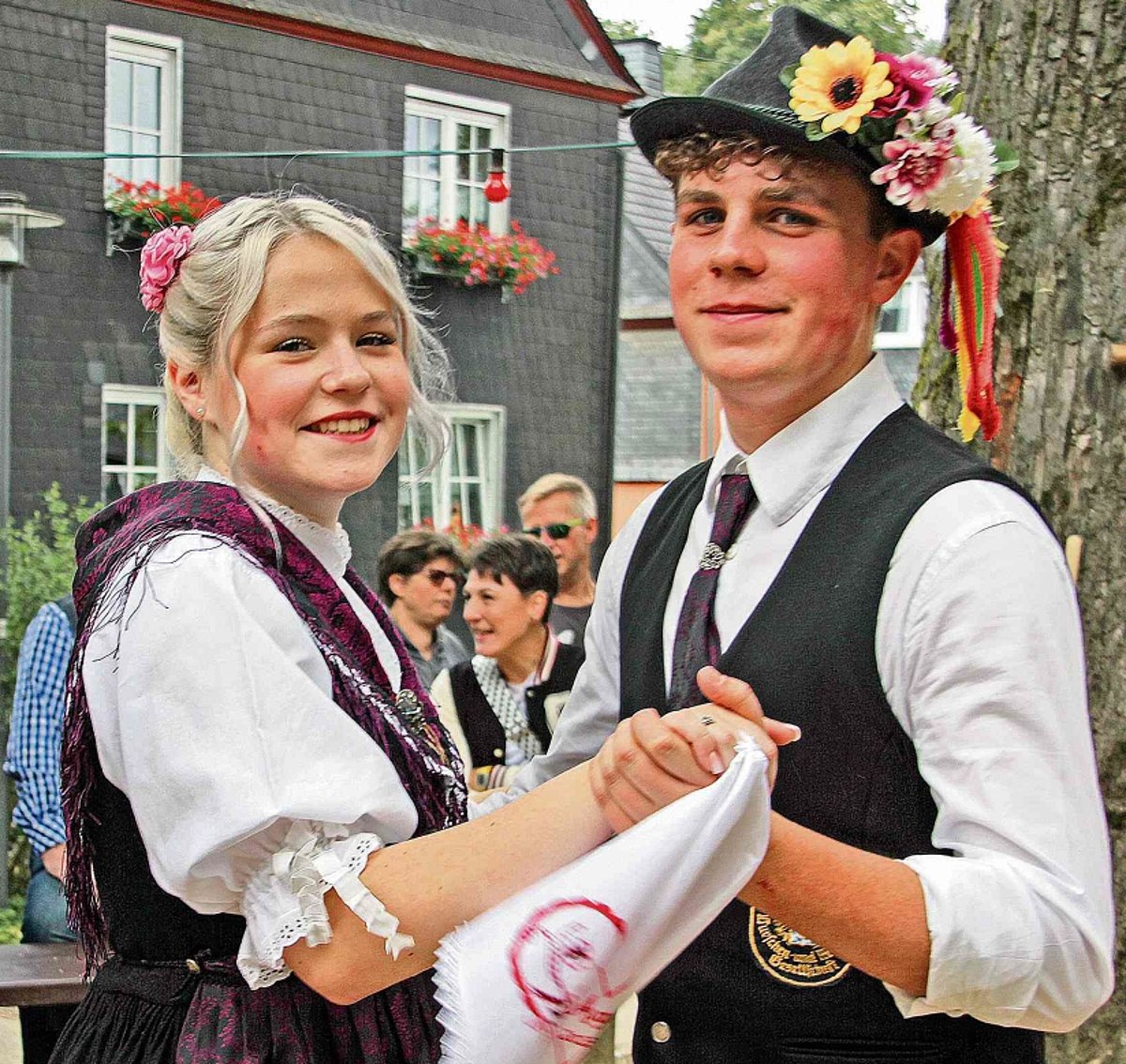 Das Foto zeigt ein Kirchweihpaar in Tracht. Beide schauen in die Kamera. Der Mann trägt einen Hut mit Blumenschmuck, das Mädchen hat ein weißes, besticktes Taschentuch in der rechten Hand. Sie stehen in Tanzstellung.