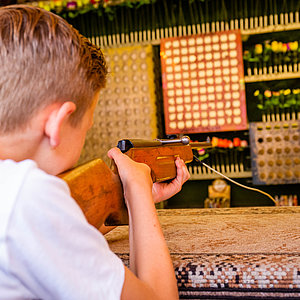 Das Bild zeigt einen Jungen, der mit einem Luftgewehr auf die Ziele in der Schießbude zielt. 