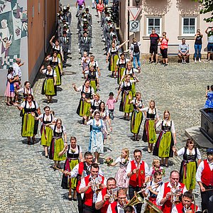 Hinter der Ebersdorfer Blaskapelle laufen die Schützendamen in ihren prächtigen Trachten. Diese bestehen aus weißen Blusen, langen schwarzen Röcken und intensiv grünen Schürzen mit verschieden farbigen Bändern. 