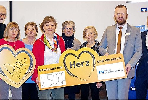 Eine Gruppe von Frauen und Männern. Alle stehen nebeneinander, halten Gutscheine in der Hand und schauen in die Kamera.