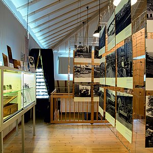 Im Foto sieht man einen Teil der Sonderausstellung mit zahlreichen Schwarz-Weiß-Fotos und beleuchteten Vitrinen.