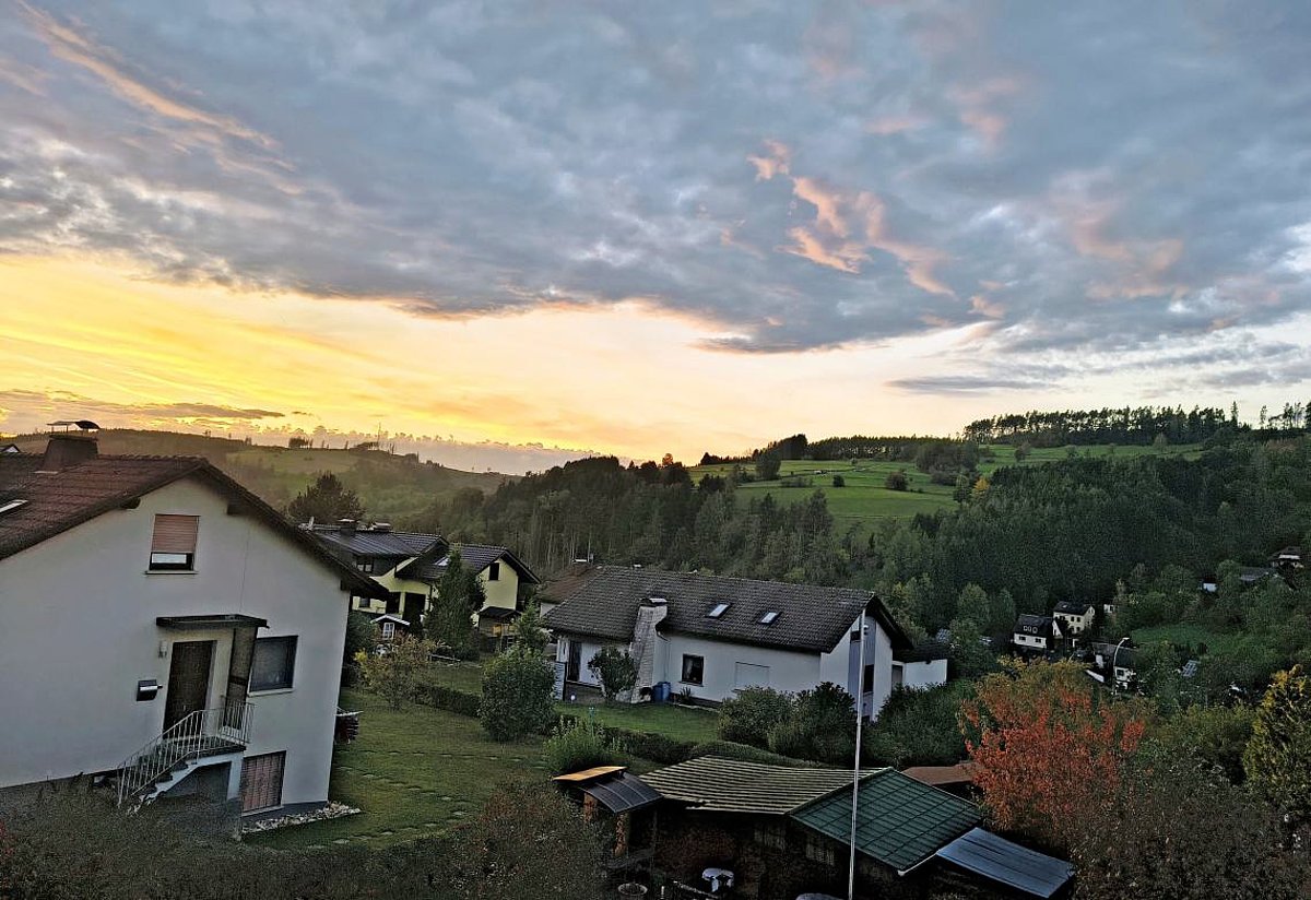 Blick über eine Einfamilienhaussiedlung im Abendlicht. Der Himmel ist teilweise mit grauen, rosaleuchtenden Wolken behangen. Im Hintergrund ist der Himmel rotgolden.