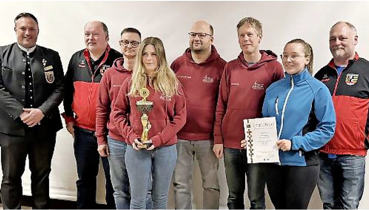 Eine Gruppe von Menschen, darunter zwei Frauen. Eine hält einen goldfarbenen Pokal, die andere eine Urkunde in ihren Händen. Alle lächeln in die Kamera.