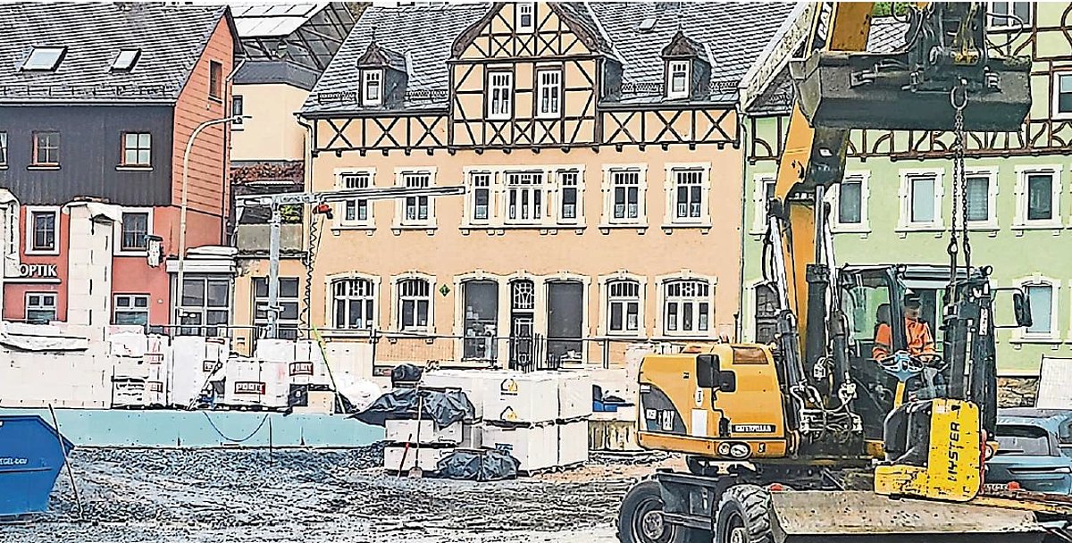 Eine Baustelle mit Kran im Vordergrund. Dahinter sind Mehrfamilienhäuser an einer Straße zu sehen.