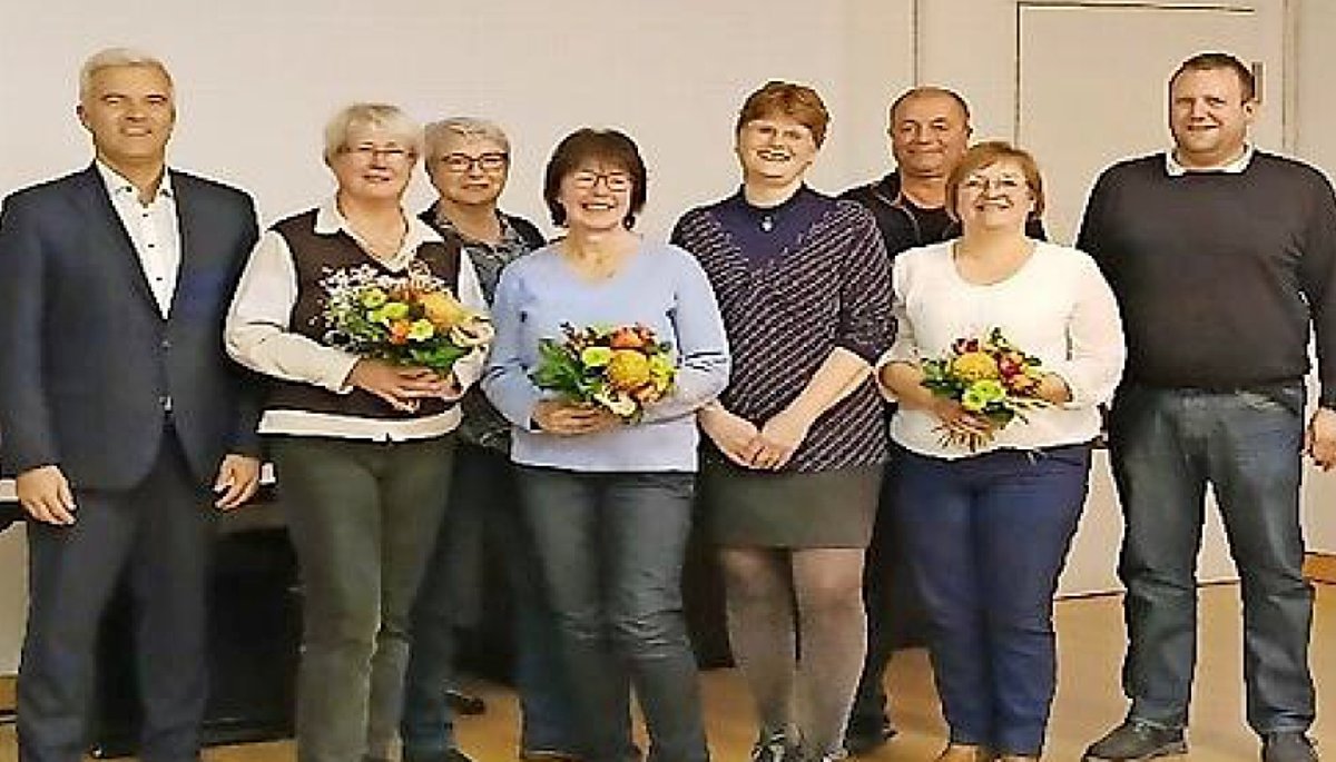 Eine Gruppe von Menschen stehen zusammen. Drei Frauen halten je einen Blumenstrauß.
