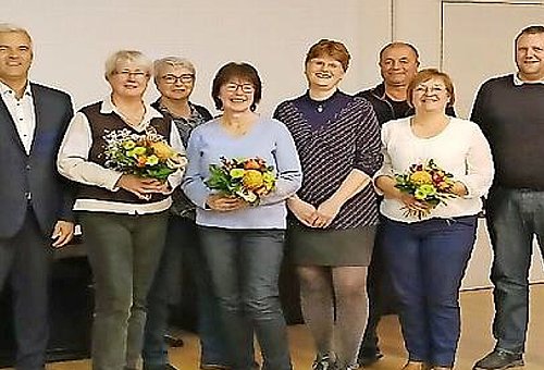 Eine Gruppe von Menschen stehen zusammen. Drei Frauen halten je einen Blumenstrauß.