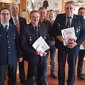 Eine Gruppe von Männern in Feuerwehruniform. Einige halten eine Urkunde in der Hand.