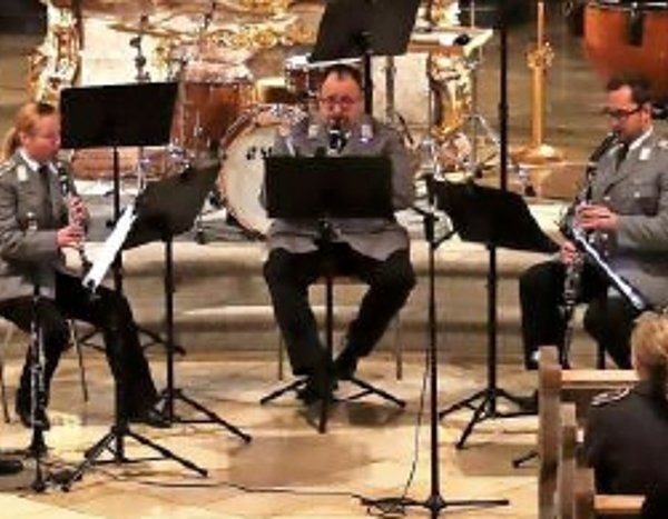 Das Bild zeigt einen Teil des Heeresmusikkorps in Uniform während eines Konzertes. Jeder spielt sein Instrument und schaut in seine Notenblätter.