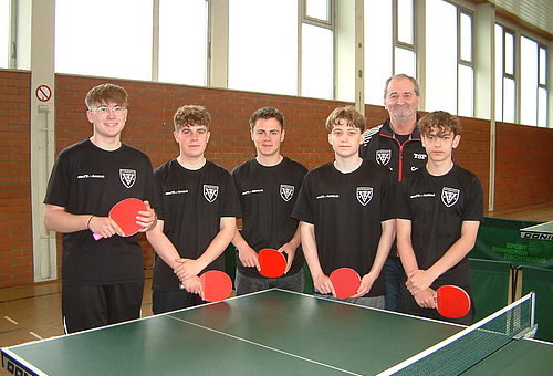 Auf dem Bild sind 5 Jungen mit Tischtennisschlägern zu sehen. Dahinter steht ihr Trainer.