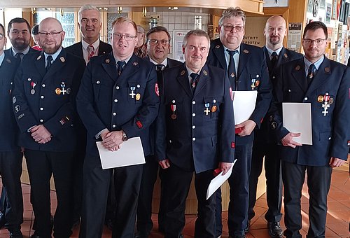 Eine Gruppe von Männern in Feuerwehruniform. Einige halten eine Urkunde in der Hand.