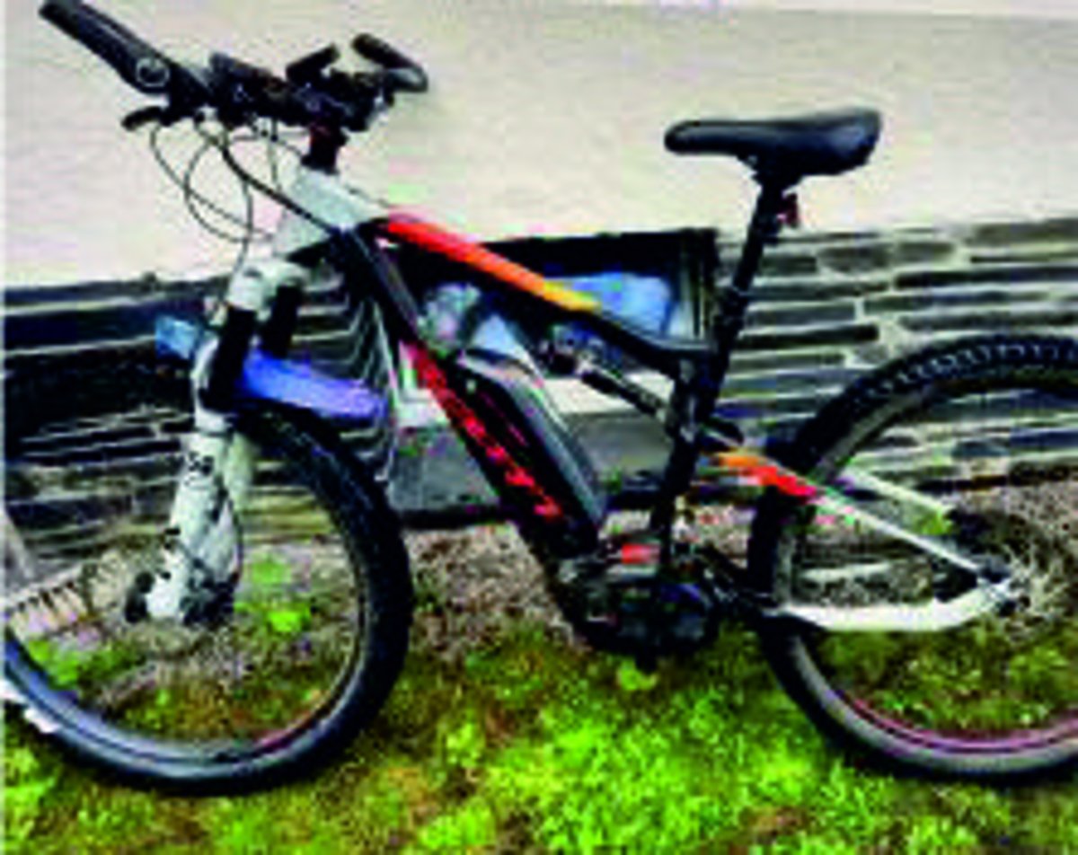 Vor einer Hauswand steht das E-Bike der Marke "Scott" mit schwarzer Grundfarbe und leuchtend hellen Farben am Rahmen.