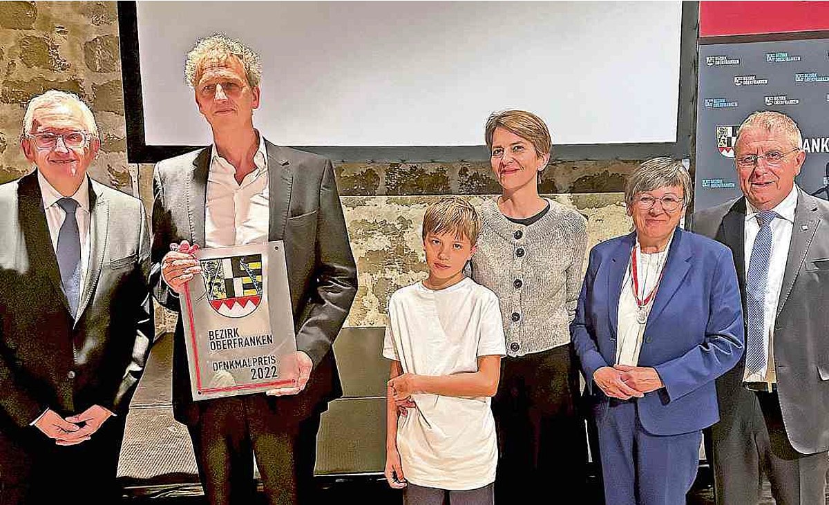 Im Foto zu sehen sind der Geehrte mit seinem Sohn und seiner Frau. Umrahmt werden Sie von dem Bezirksheimatpfleger, der Regierungspräsidentin und dem Bezirkstagspräsidenten. Alle Personen sind festlich gekleidet.
