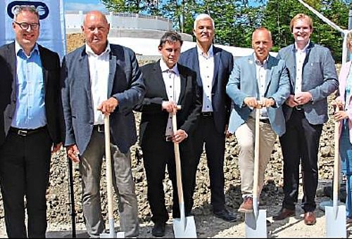 Eine Gruppe von Menschen steht in einer Reihe nebeneinander. Einige der Männer halten einen Spaten in der Hand. Alle lächeln in die Kamera.