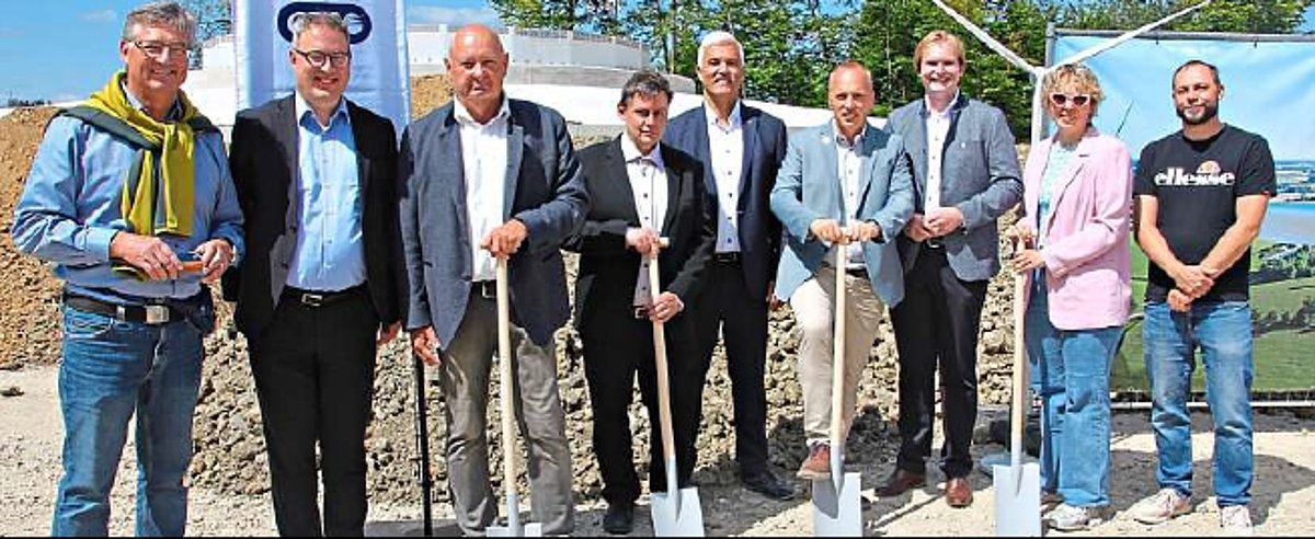Eine Gruppe von Menschen steht in einer Reihe nebeneinander. Einige der Männer halten einen Spaten in der Hand. Alle lächeln in die Kamera.