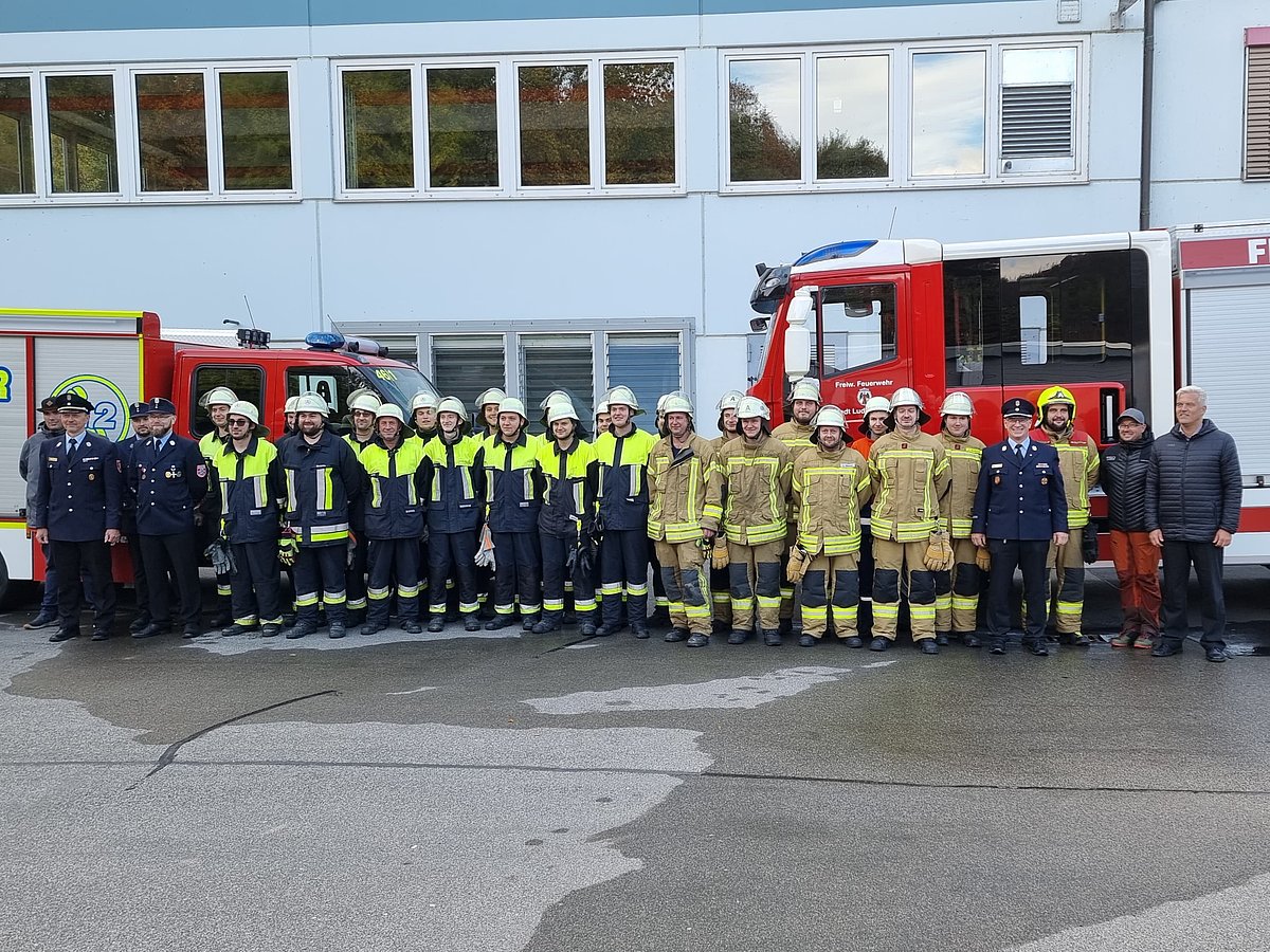 Feuerwehrleute in verschiedenen Uniformen stehen vor ihren Fahrzeugen und schauen in die Kamera.