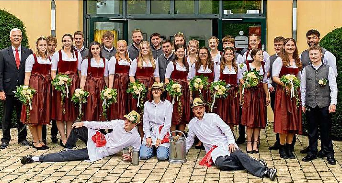 In zwei Reihen steht die Kirchweihgesellschaft. In der ersten Reihe stehen die jungen Frauen in roten Dirndln mit roten Schürzen und weißen Blumen. Jede hält einen Blumenstrauß. Die Burschens stehen dahinter. Sie tragen graue Westen, schwarze Hosen und weiße Hemden. Vor der Gruppe liegen zwei Männer (die Kellner) und dazwischen kniet eine Frau (ebenfalls Kellner). An der linken Seite der Gruppe steht Bürgermeister Timo Ehrhardt.