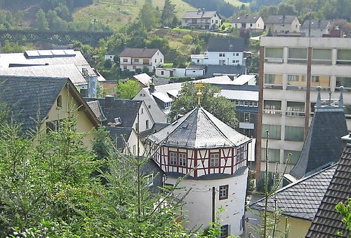 Blick auf die Stadt. Zentral ist ein rundes Gebäude mit Fachwerk und Schieferdach zu sehen. 
