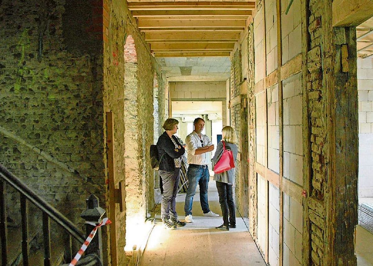 In einem Gebäude stehen zwei Frauen und ein Mann ins Gespräch vertieft. Um sie herum sind unverputzte Wände einer Baustelle zu sehen.