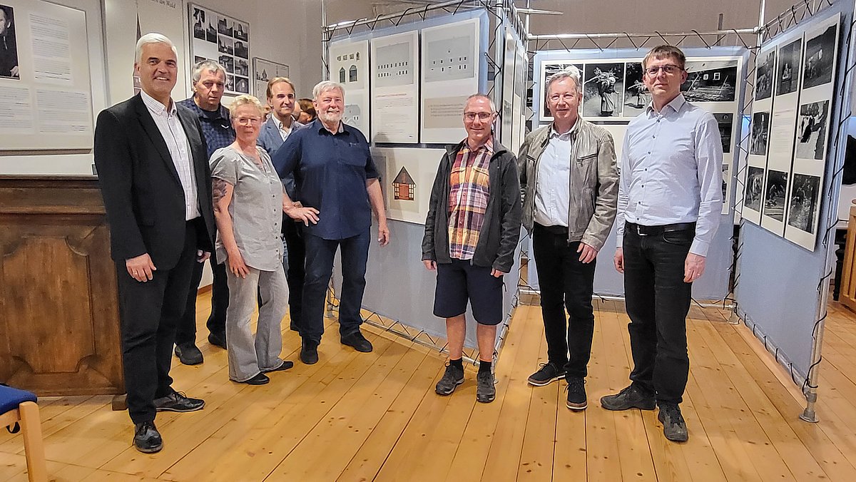 In einem Raum mit Wänder voller Fotografien stehen eine Gruppe von Menschen. Darunter ein Frau und der Bürgermeister Timo Ehrhardt. Alle schauen in die Kamera.