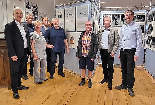 In einem Raum mit Wänder voller Fotografien stehen eine Gruppe von Menschen. Darunter ein Frau und der Bürgermeister Timo Ehrhardt. Alle schauen in die Kamera.