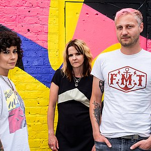 zwei Frauen und ein Mann stehen vor einer bunt bemalten Steinwand