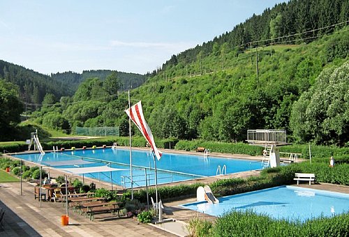 Das Freibad mit einem großen Schwimmerbecken und einem Kleinkindbecken. Umrahmt ist das Bad von dichten Wäldern. 