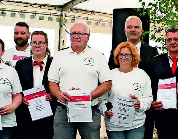 Auf dem Bild sind Männer und Frauen der BRK-Bereitschaft Lauenstein mit weißen T-shirts zu sehen, die ihre Urkunde in den Händen halten. Links und rechts davon stehen die Ehrengäste.