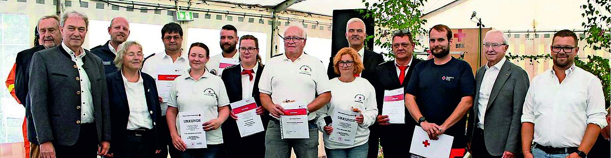 Auf dem Bild sind Männer und Frauen der BRK-Bereitschaft Lauenstein mit weißen T-shirts zu sehen, die ihre Urkunde in den Händen halten. Links und rechts davon stehen die Ehrengäste.