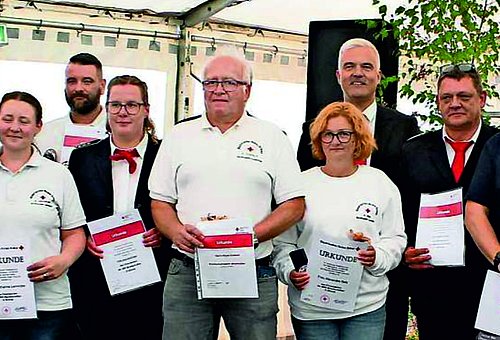 Auf dem Bild sind Männer und Frauen der BRK-Bereitschaft Lauenstein mit weißen T-shirts zu sehen, die ihre Urkunde in den Händen halten. Links und rechts davon stehen die Ehrengäste.