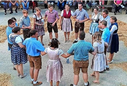 Das Foto zeigt den Tanzanger mit der Kirchweihgesellschaft. Die Damen tragen Dirndl, die Männer Lederhosen. Sie stehen in einem großen Kreis.