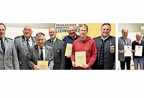 Eine Gruppe von Menschen stehen zusammen und lächeln in die Kamera. Sie tragen dunkelgraue Schützenuniformen und schwarze Anzüge. Sechs von ihnen halten je eine Urkunde in ihren Händen.