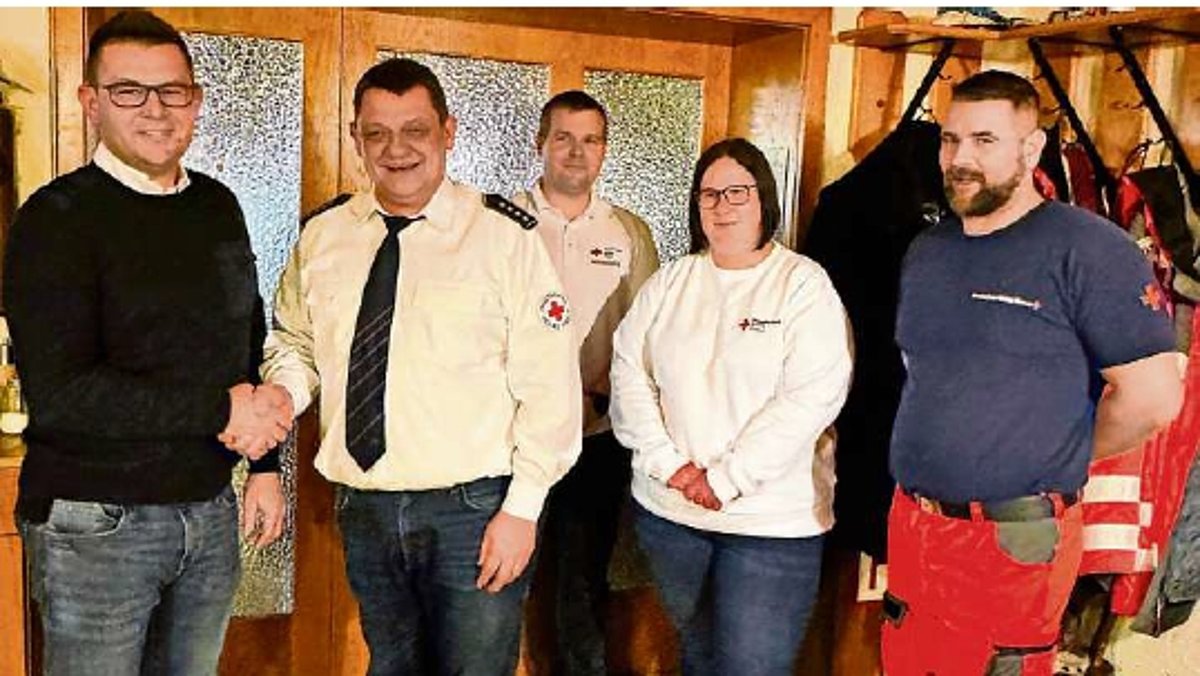 Vier Männer und eine Frau stehen in einer Gruppe. Zwei Männer drücken sich die Hände. Alles schauen in die Kamera und lächeln.