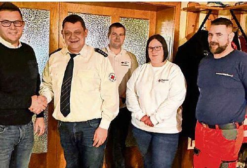 Vier Männer und eine Frau stehen in einer Gruppe. Zwei Männer drücken sich die Hände. Alles schauen in die Kamera und lächeln. 