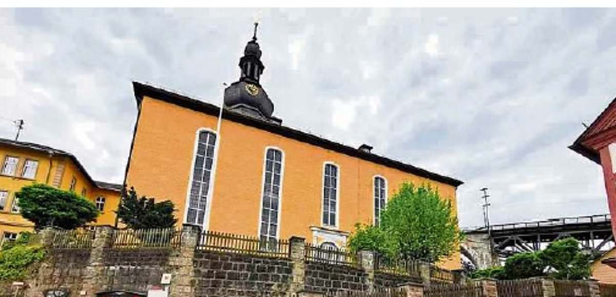 Eine Kirche, die hoch über den Fotografen ragt, hat eine orange-gelbe Fassade und einen geschieferten Turm.