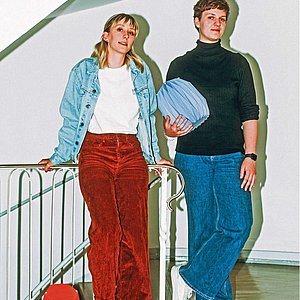 zwei Frauen stehen in einem Treppenhaus, eine hält eine Papierurne in der Hand, eine zweite Urne steht zu Füßen der Frauen