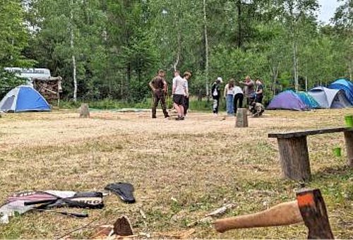 Das Foto zeigt einen Zeltplatz mit einer Gruppe von Jugendlichen im Hintergrund.