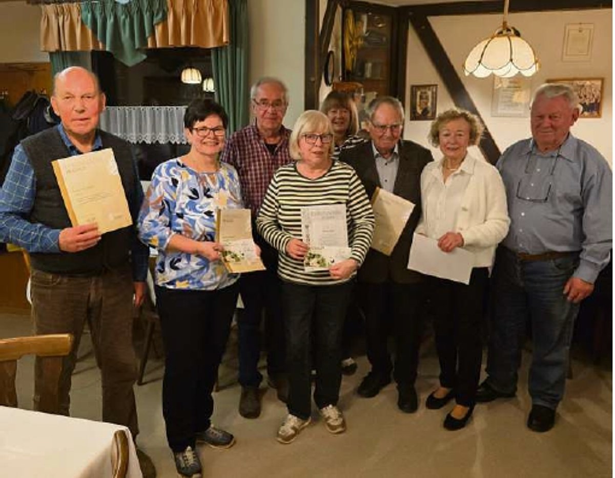 In einem Raum steht eine Gruppe von Männern und Frauen in Alltagskleidung. Einige halten eine Urkunde in ihren Händen.