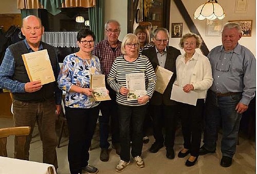 In einem Raum steht eine Gruppe von Männern und Frauen in Alltagskleidung. Einige halten eine Urkunde in ihren Händen.