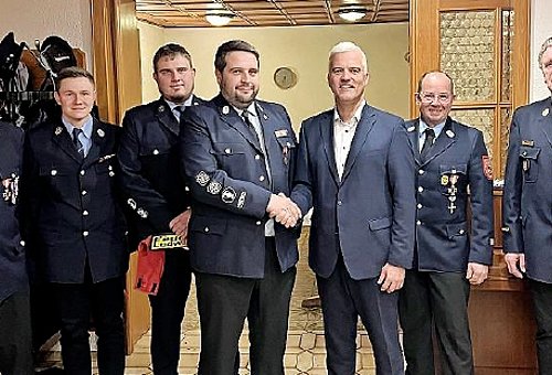 Die Mitglieder der Feuerwehr stehen in Uniform in einer Reihe. Es sind alles Männer. Vorn reicht Bürgermeister Timo Ehrhardt einem uniformierten Mann die Hand zur Gratulation.