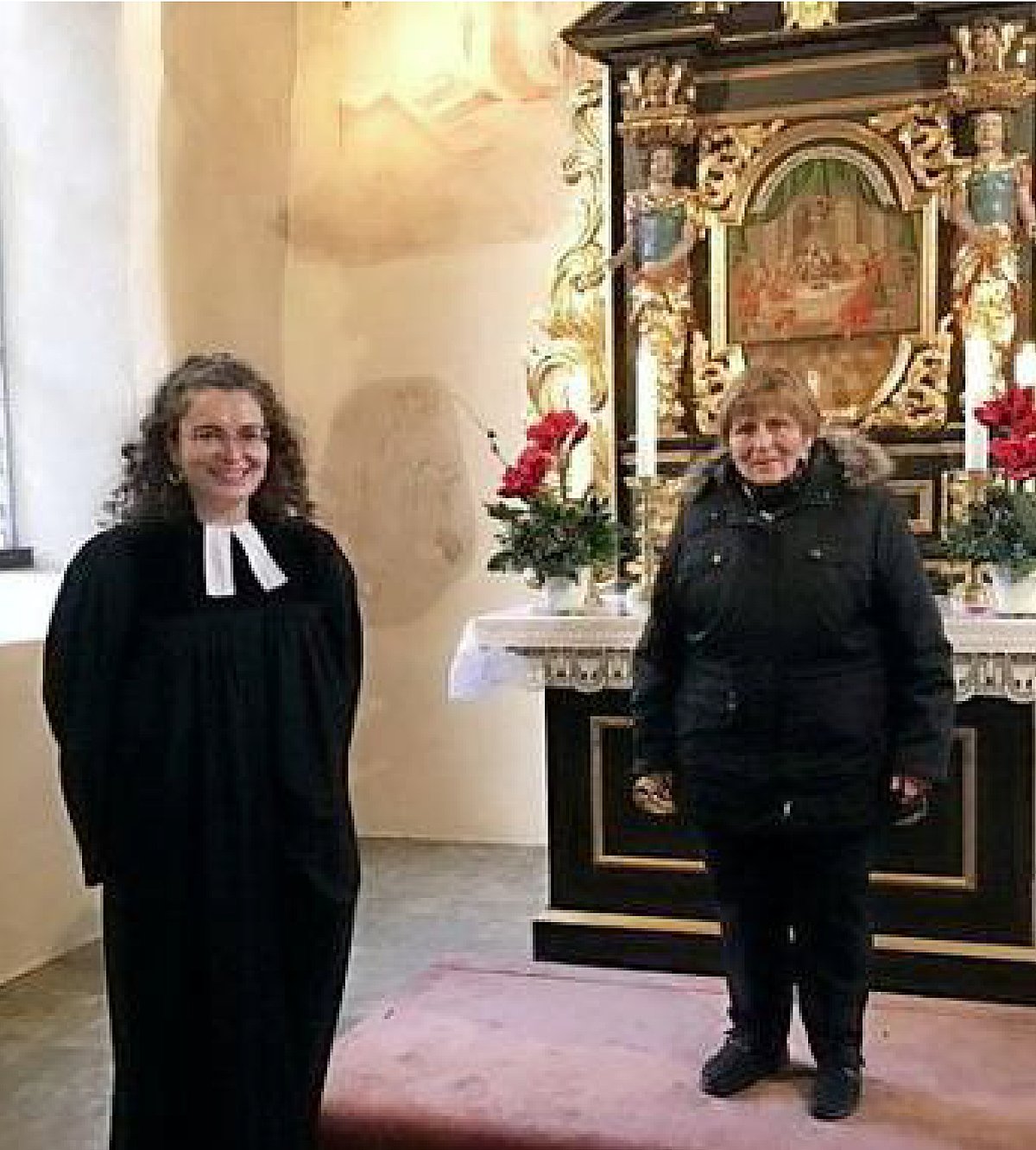 Pfarrerin und eine Seniorin stehen mit Abstand vor einem Kirchenaltar