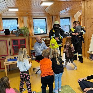 Kindergartenkinder und Feuerwehrmänner in Uniform. Sie üben spielerisch für den Ernstfall