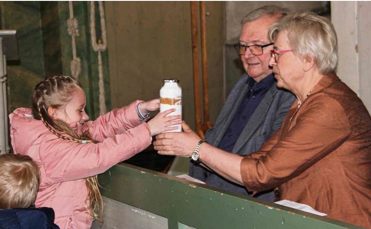 Ein Mädchen übergibt ein Geschenk an eine Frau. Neben ihr sitzt ihr Ehemann.