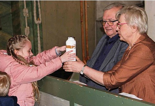 Ein Mädchen übergibt ein Geschenk an eine Frau. Neben ihr sitzt ihr Ehemann.
